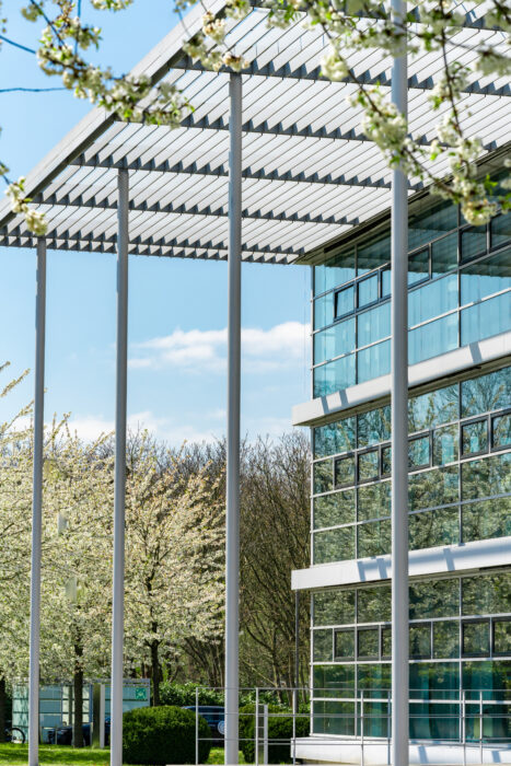 Gläsernes Bürogebäude mit blühenden Bäumen und Spiegelung von blauem Himmel.
